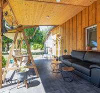 The terrace of a family house in Tvrdošovce with wooden paneling, a swinging bench, and a black sofa.