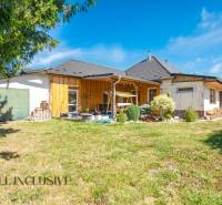 A family house in Tvrdošovce with wooden cladding, a garden, and a view of the blue sky.