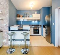 A kitchen in a 3-room apartment with a gray refrigerator and bar stools.