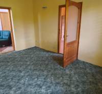 A room in a family house with yellow walls and a green carpet, open doors to the sofa.