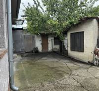 A family house in Dobrohošť with a garden shed, a tree, and a wheelbarrow on a concrete yard.