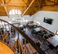 Gastro premises with a wooden ceiling, chandelier, and metal railing, comfortable seating at tables.