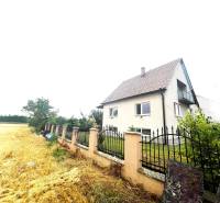 A family house in Veľké Chlievany near a field with a fence and a garden in the background.