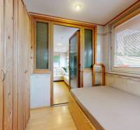 A narrow room with a wooden wardrobe, a bed, and sliding doors to the living area.