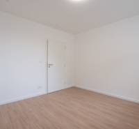 An empty room with wooden flooring and white walls in a 3-bedroom apartment.