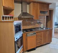 A kitchen with wooden cabinets in a 3-room apartment, containing a stove and a dishwasher.