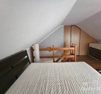 Attic bedroom with a sloped ceiling in a 3-room apartment, with a wooden railing and a dresser.