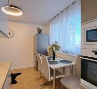 A kitchen in a 2-room apartment with wooden flooring, a dining table, and built-in appliances.