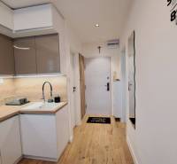 A kitchen in a 2-room apartment with white cabinets, a wooden countertop, and a large clock.