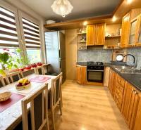 A kitchen with a table and chairs in a four-room apartment, wooden cabinets, windows with flowers.