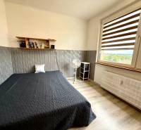 A bedroom in a 4-room apartment with a bed, shelf, fan, and large window.