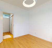 An empty room in a 2-room apartment with white walls, wooden floor, and a vase with flowers.
