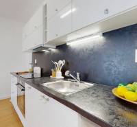 A kitchen with a dark countertop, white cabinets, and a bowl of fruit, 2-room apartment.