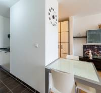 A kitchen with a dining area, a clock on the wall, and storage space in a studio apartment.