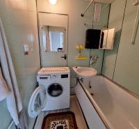 Bathroom in a 3-room apartment with a washing machine, bathtub, and mirror on the wall.