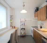 A kitchen with wooden cabinets, a gas stove, and white seating in a 3-room apartment.