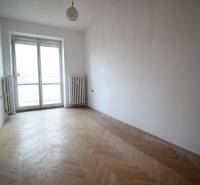 An empty room with parquet flooring in a 3-room apartment, with a large window and radiators.