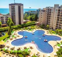 A holiday apartment on the Sunny Beach with a pool surrounded by modern buildings and a sea view.