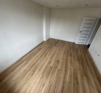 An empty room with wooden flooring and white walls in a 2-bedroom apartment.