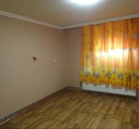 A room in a family house with a wooden floor and orange curtains with a children's motif.