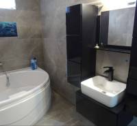 A bathroom in a family house with a corner bathtub and black cabinets.