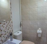Bathroom in a studio apartment with light tiles and a toilet, sink with a faucet.