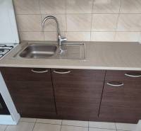 Kitchen in a studio apartment with a stove, sink, and washing machine, light tiled wall.