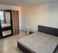 Bedroom in a one-room apartment with a double bed, wardrobe, and glass table.