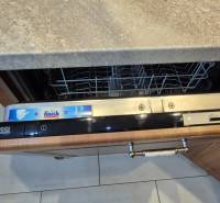 An open Zanussi dishwasher in a studio apartment with a wooden kitchen interior.
