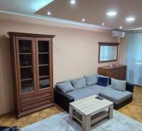 Living room in a studio apartment with a sofa and wooden furniture, illuminated by spotlights.