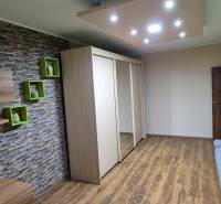 Living area of a studio apartment with a stone wall, mirrored wardrobe, and sofa.
