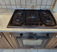 A kitchen with a gas stove and oven in a studio apartment, wooden cabinets, and tiled backsplash.