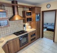 A kitchen in a studio apartment with wooden cabinets, a range hood, and built-in appliances.