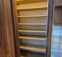 A pantry with shelves in a one-room apartment with a wooden door frame and tiles.