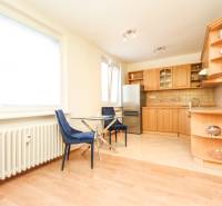 A kitchen in a 2-room apartment with a wooden cabinet, blue chairs, and large windows.