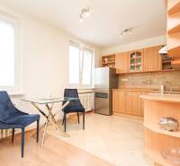A kitchen in a 2-room apartment with wooden cabinets and a table with two blue chairs.