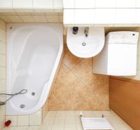 A bathroom with a bathtub, sink, and washing machine in a 2-room apartment.