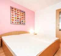 A bedroom in a two-room apartment with a bed, a pink wall, and a picture of hearts.