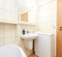 A bathroom in a 2-room apartment with a sink, a washing machine, and a mirror.