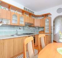 A kitchen in a 3-room apartment with a wooden cabinet, a dining table, and access to the balcony.