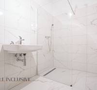 A bathroom in a family house with a sink and a shower, featuring predominantly white tiles.