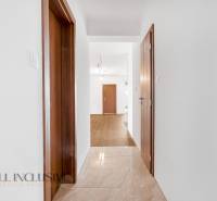 A hallway in a family house with white walls, wooden doors, and tiled flooring.