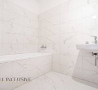 A bathroom with a bathtub and a sink in a family house, tiled with light ceramic tiles.