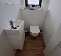 A small bathroom with a sink and toilet in a family house, complemented by a wooden floor.