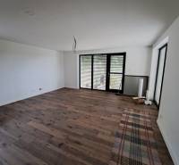 A room in a family house with a wooden floor and large windows with blinds.