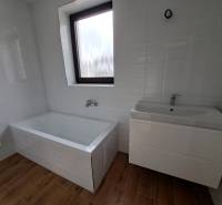 A bathroom in a family house with a bathtub and a sink on a wooden floor.