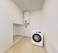 Laundry room in a family house with a washing machine and a boiler, white walls, tiles.