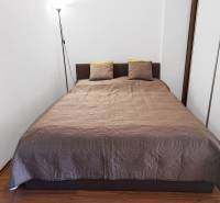 Bedroom with a double bed and a lamp in a 2-room apartment, simple design, wooden floor.