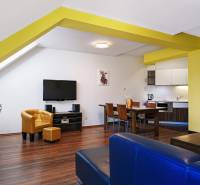Living room in a two-room apartment with wooden flooring, a yellow wall, and a television.