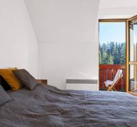 Bedroom of a 2-room apartment with a view of the forests through an open balcony.